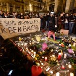 People holding a banner reading "I am Brussels" behind flowers and candles to mourn for the victims at Place de la Bourse in the center of Brussels, Tuesday, March 22, 2016. Bombs exploded at the Brussels airport and one of the city's metro stations Tuesday, killing and wounding scores of people, as a European capital was again locked down amid heightened security threats.