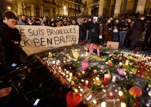 People holding a banner reading "I am Brussels" behind flowers and candles to mourn for the victims at Place de la Bourse in the center of Brussels, Tuesday, March 22, 2016. Bombs exploded at the Brussels airport and one of the city's metro stations Tuesday, killing and wounding scores of people, as a European capital was again locked down amid heightened security threats.