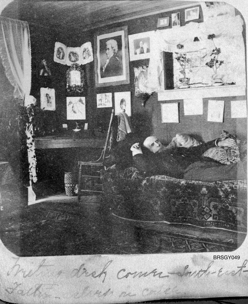 Writing desk corner – south-east / Father asleep on couch circa 1898-1900. This room was probably on the second floor of the two-story Bracketts Trading Post, otherwise known as the Mansion House, located on the northwest corner of 3rd Avenue and Main Street in Skagway. (Courtesy Photo | National Park Service, Klondike Gold Rush National Historical Park, Brackett Family Collection, BRSGY049, KLGO BI-45-5246)