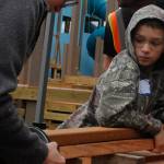 Eli Harvey, 10, holds a piece of lumber and watches as his mom Stephanie Harvey sands it at Project Playground on Wednesday, Aug. 8, 2018. (Alex McCarthy | Juneau Empire)