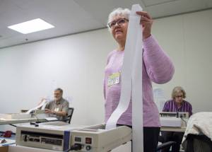 Laraine Derr, of the Regional Accu-Vote Board, center, waits for her machine to print out a tally as she, David Clover, left, and Mary Foster count questioned and absentee ballots at the State of Alaska election office at the Mendenhall Mall on Tuesday, Aug. 28, 2018. (Michael Penn | Juneau Empire)