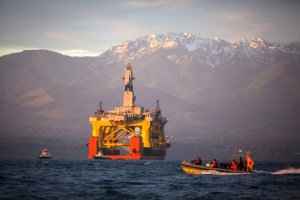 In this April 2015 file photo, with the Olympic Mountains in the background, a small boat crosses in front of an oil drilling rig as it arrives in Port Angeles, Washington, aboard a transport ship after traveling across the Pacific. Royal Dutch Shell PLC confirmed Tuesday it will relinquish all but one of its federal offshore leases in Alaska's Chukchi Sea.