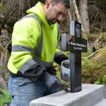 JR Lindstrom, a close friend of the Diaz brothers, cements a cross – with the engraved photos of Elmer and Ulises – in place near a memorial bench Wednesday evening. More than 200 people gathered for the dedication of  the bench and cross Thursday afternoon at the head of the Cross Trial near Kramer Avenue. The bench, which affords views over Sitka Sound and Mt. Edgecumbe, was dedicated to the memory of Elmer and Ulises Diaz and William Stortz who died in the Aug. 18, 2015, landslide on Kramer Avenue.