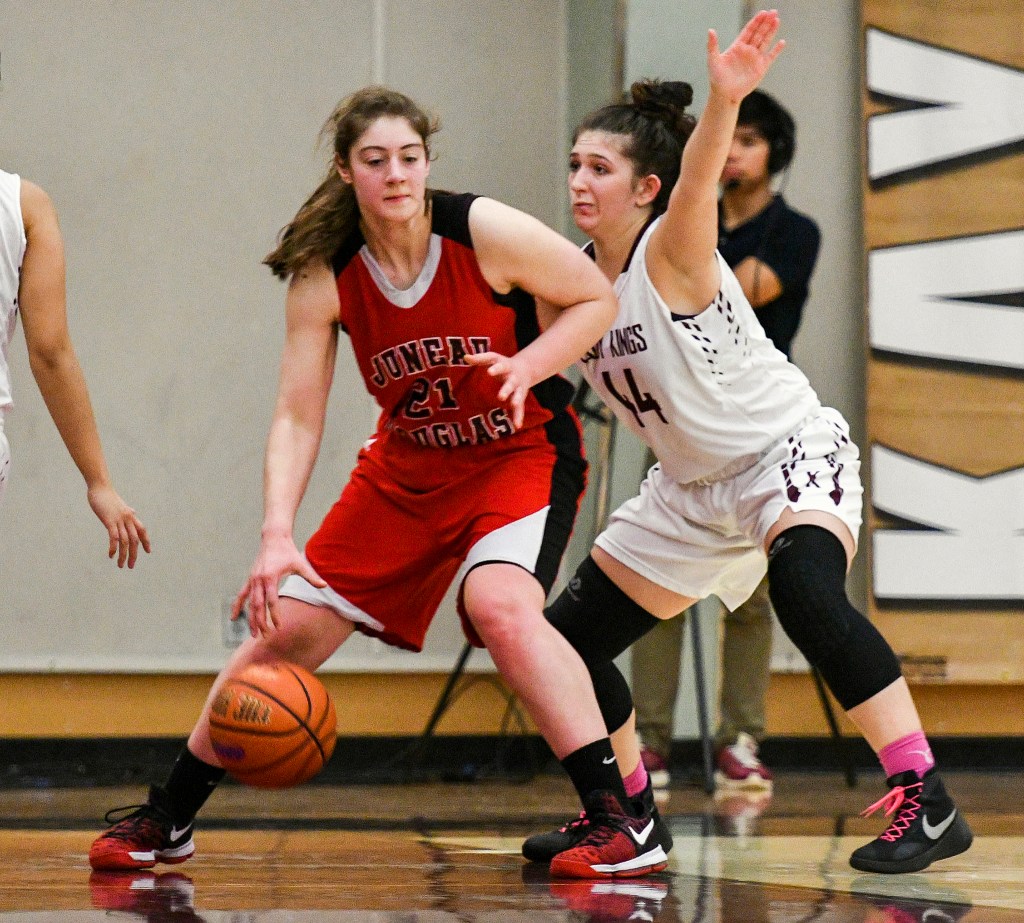 Juneau-Douglas High School junior Cassie Dzinich (21) dribbles the ball around Ketchikan High School senior Kyra Welker (44) on Friday during the Crimson Bears&rsquo; 56-39 win against the Lady Kings. (Taylor Balkom | Ketchikan Daily News)