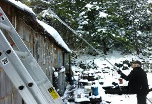 Tara Neilson&rsquo;s dad, Gary, scrapes snow off the roof. Behind him the picnic table and a chair on her parents&rsquo; front deck, which Tara swept earlier, are once again covered. Photos by Tara Neilson.