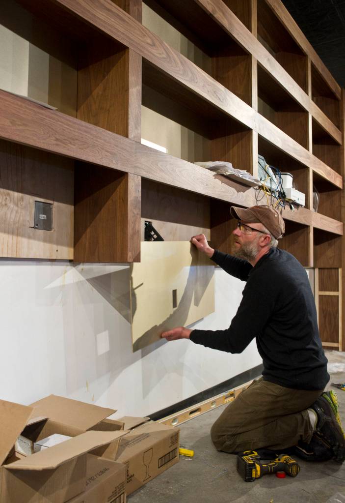 Jake Lapenter works under new walnut shelving at the new bar called The Narrows on Thursday. The bar opens to the public on Monday. (Michael Penn | Juneau Empire)