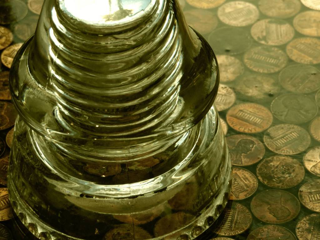 A glass wire insulator on a counter top covered with copper pennies. Photo by Ray Tsang.