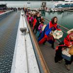 Hoonah City School students drum their way up the dock to greet the waiting totem poles. (Mary Beth Moss | For the Capital City Weekly)