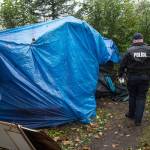 Juneau Police Department Officers serve eviction notices on homeless encampments as Alaska Mental Health Trust Authority employees look on on Tuesday, Aug. 22, 2017. (Michael Penn | Juneau Empire)