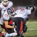 Juneau-Douglas&rsquo; Donavin McCurley has his helmet knocked off by North Pole&rsquo;s C J Fontana, left, and Jacob Pflughoeft at Adair-Kennedy Memorial Field on Saturday, Sept. 23, 2017. JDHS lost 16-22. (Michael Penn | Juneau Empire)