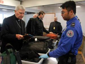 Transportation Security Officer Renier Cava gives instructions to Father Roger Schwietz on Wednesday, Oct. 11 at the Juneau International Airport. A new policy from the Transportation Security Administration requires passengers to remove all electronic items larger than their cell phones and put them through the scanner. (Alex McCarthy | Juneau Empire)