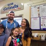 Erik Scholl with his partner, Tianna Banua, and their children Ezra and Ezlyn Vidal, stand in front of one of their two food businesses in the State Office Building on Thursday, Nov. 9, 2017. They operate SOB Grinds and Shaka Shack, both located on either end of the eighth floor atrium. (Michael Penn | Juneau Empire)