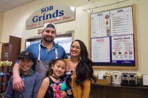 Erik Scholl with his partner, Tianna Banua, and their children Ezra and Ezlyn Vidal, stand in front of one of their two food businesses in the State Office Building on Thursday, Nov. 9, 2017. They operate SOB Grinds and Shaka Shack, both located on either end of the eighth floor atrium. (Michael Penn | Juneau Empire)