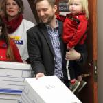 Rep. Jason Grenn, I-Anchorage, carrying his son Truman, and Joelle Hall carry boxes containing more than 45,000 signatures into the Alaska Division of Elections office in Anchorage, Alaska, Friday, Jan. 12, 2018. Elections workers will have to verify the signatures before the measure is approved for the ballot. (Mark Thiessen | The Associated Press)