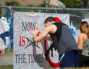 A man signs a banner as people pay tribute at a memorial for the victims of the shooting at Marjory Stoneman Douglas High School on Sunday, Feb. 25, 2018, in Parkland, Fla. Thousands of students joined their parents in walking past the three-story building at the Florida high school where the Feb. 14 shooting took place. It is now cordoned off by a chain link fence that was covered with banners from other schools showing their support. (David Santiago/Miami Herald via AP)