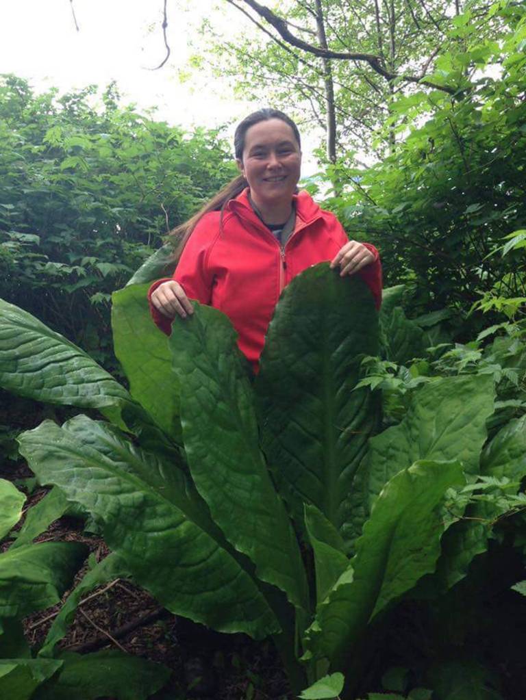 Vivian Mork, Vivian Prescott&rsquo;s daughter and co-writer of Planet Alaska, stands by skunk cabbage leaves. Image courtesy of Vivian Faith Prescott.
