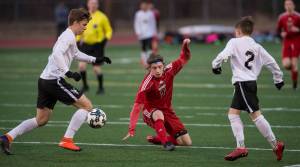 Juneau-Douglas&rsquo; Jackson Norberg punches the ball between West Anchorage&rsquo;s Dominic Owen, left, and Jack Nelson, right, at Adair-Kennedy Memorial Park on Friday, April 20, 2018. West won 3-1. (Michael Penn | Juneau Empire)