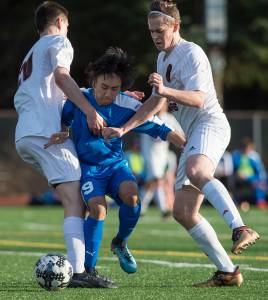 Thunder Mountain&rsquo;s Marc Manlulu is pinned between Juneau-Douglas&rsquo; Ben Campbell, left, and Tulio Fontanella at Adair-Kennedy Memorial Park on Tuesday, May 8, 2018. The game ended in a 2-2 tie. (Michael Penn | Juneau Empire)