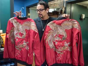 Gabriel Rivera, of 4th Coast Outfitters, holds up a pair of embroidered phoenix bomber jackets on Wednesday, May 16, 2018, he thinks will be worn in this weekend&rsquo;s Flappers Fashion show. (Michael Penn | Juneau Empire)
