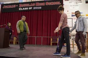 Henry Cheng, a graduating senior at Juneau-Douglas High School, practices walking across the stage at JDHS with the help of his father, Vincent, second from left, para educator Valerie Cables, right, and physical therapist Che Plang, of Southeast Alaska Therapies, on Thursday, May 24, 2018, in preperation of Sunday&rsquo;s graduation ceremony. Henry suffered a severe traumatic brain injury after falling off a cliff in 2016. (Michael Penn | Juneau Empire)