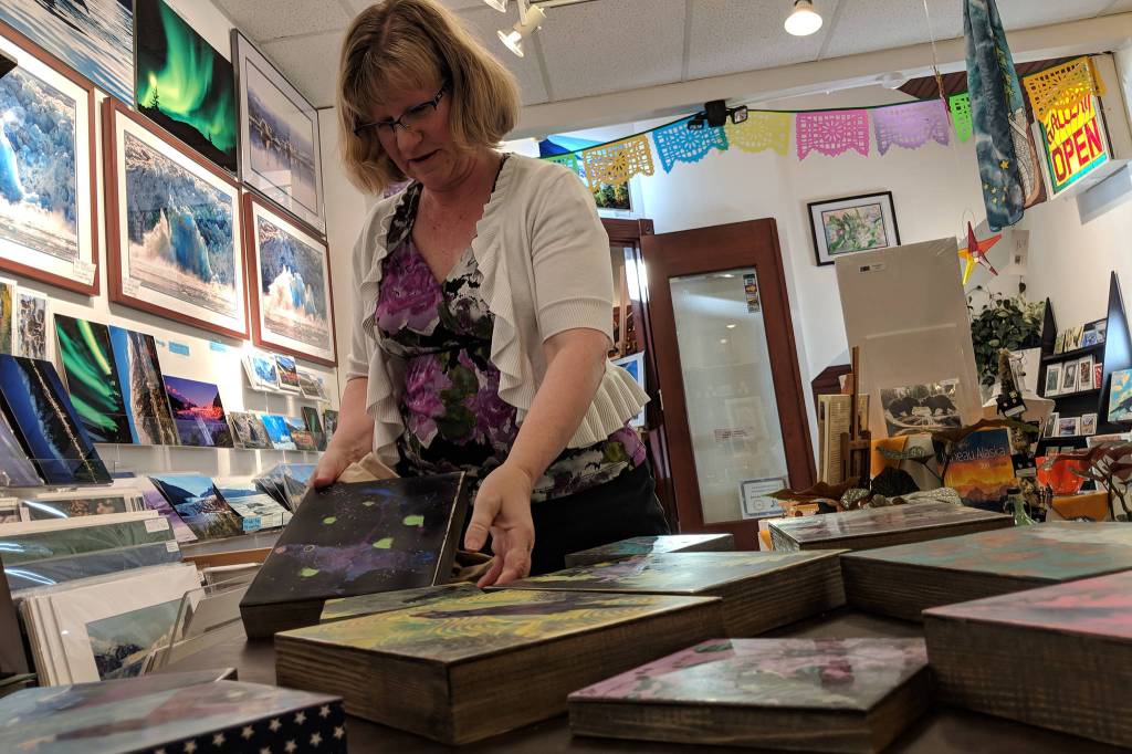 Dorolyn Alper picks up one of her encaustic pieces at the Juneau Artists Gallery. Alper is the artist of the month at the gallery, and her work is on display. Alper is a multimedia artist who also works with text tiles. Her most recent work is 10 encaustic pieces depicting ravens. (Ben Hohenstatt | Capital City Weekly)