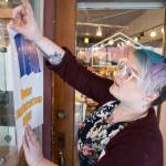 Veronica Buness, of Kindred Post, tapes up a sign on Thursday, Oct. 4, 2018, announcing people can register to vote at the Franklin Street business. (Michael Penn | Juneau Empire)