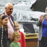 Outgoing Mayor Ken Koelsch, surrounded by his grandchildren, is acknowledged for his service by incoming Mayor Beth Weldon in a crowded Assembly chambers on Monday, Oct. 15, 2018. (Michael Penn | Juneau Empire)