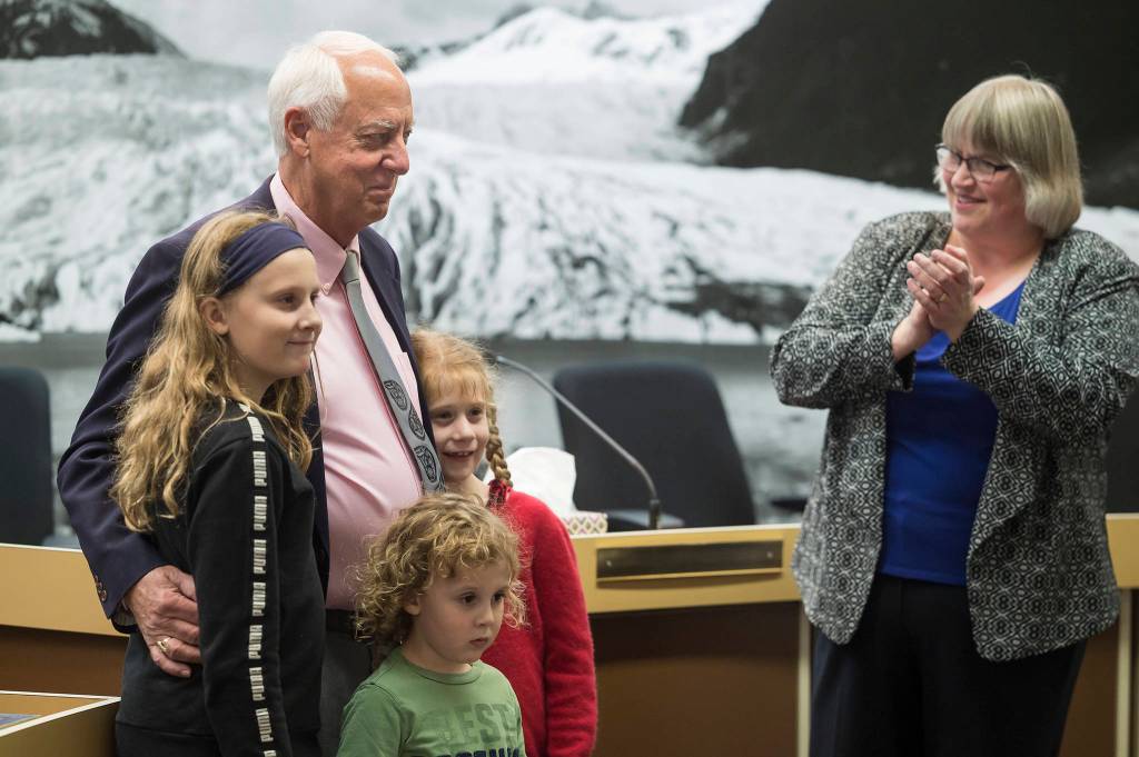 Outgoing Mayor Ken Koelsch, surrounded by his grandchildren, is acknowledged for his service by incoming Mayor Beth Weldon in a crowded Assembly chambers on Monday, Oct. 15, 2018. (Michael Penn | Juneau Empire)
