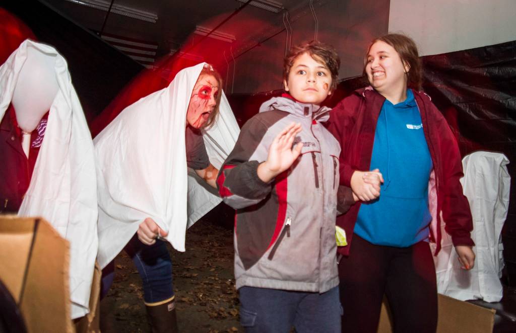 Joel Price, 11, center, and his sister, Katie, 19, are given a scare as they make their way through the Haunted Station at the U.S. Coast Guards Station Juneau on Friday, Oct. 26, 2018. Station personnel pay for all the decoration themselves and take three weeks to ready the station. Entry is non perishable food items for the Southeast Alaska Food Bank. (Michael Penn | Juneau Empire)