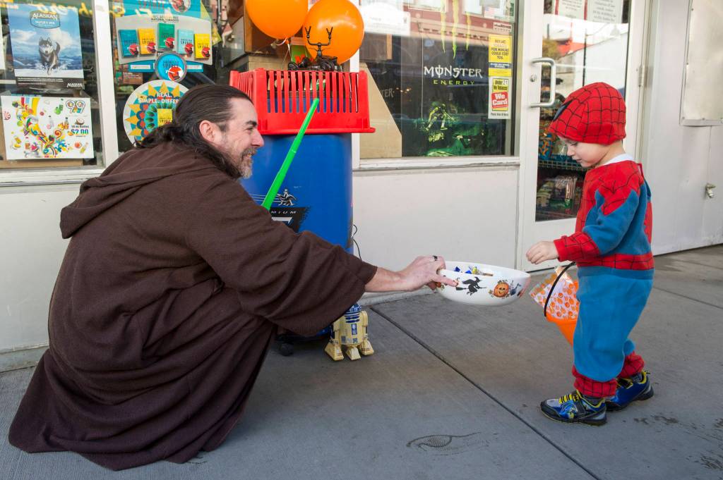 John Dahl hands out candy to Andrew Dodd, 3, in front of Alaska Cache Liquor on Wednesday, Oct. 31, 2018. For the fourth year Kindred Post has organized the Halloween celebration for trick-or-treaters. (Michael Penn | Juneau Empire)