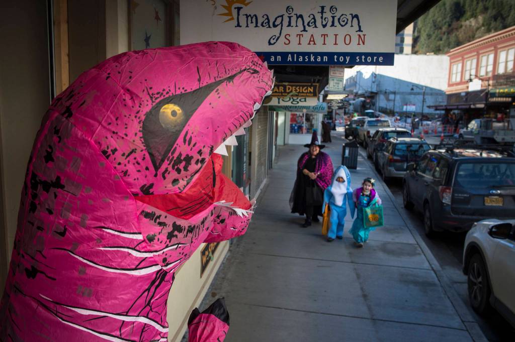 A T-Rex awaits Laura Cooper and her twins, Tanner and Amara, 5, in front of the Imagination Station on Wednesday, Oct. 31, 2018. For the fourth year Kindred Post has organized the Halloween celebration for trick-or-treaters. (Michael Penn | Juneau Empire)