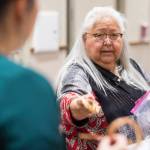 Master weaver Della Cheney hands Heather Gatti more cedar root to finish her braclett at Celebrating Our Ways of Life for Native American Heritage Month at the Elizabeth Peratrovich Hall on Friday, Nov. 16, 2018. (Michael Penn | Juneau Empire)