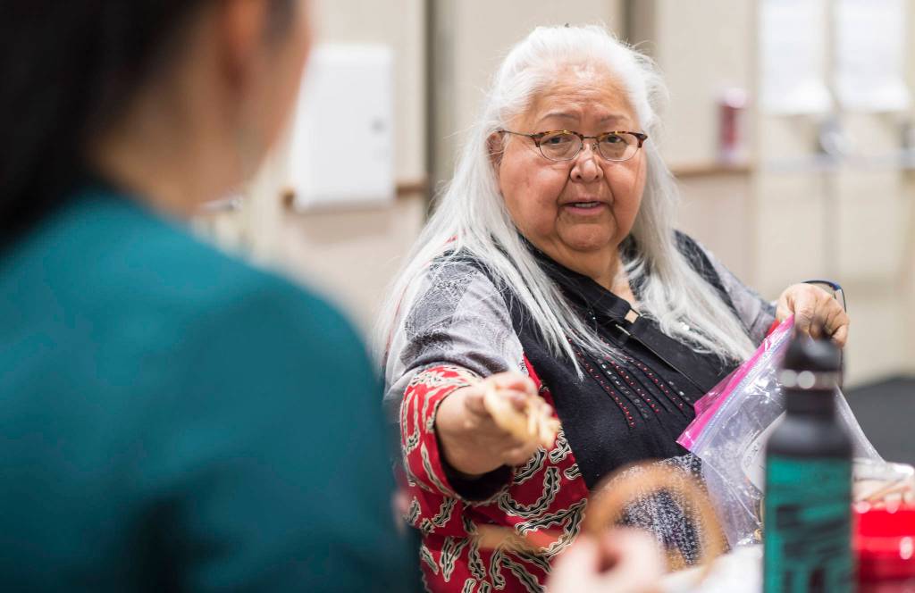 Master weaver Della Cheney hands Heather Gatti more cedar root to finish her braclett at Celebrating Our Ways of Life for Native American Heritage Month at the Elizabeth Peratrovich Hall on Friday, Nov. 16, 2018. (Michael Penn | Juneau Empire)