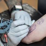 Tattoo artist Mario Singh applies a stylized semicolon to the back of Amy Ridles upper arm at Taku Tattoo on Monday, Nov. 19, 2018. (Michael Penn | Juneau Empire)