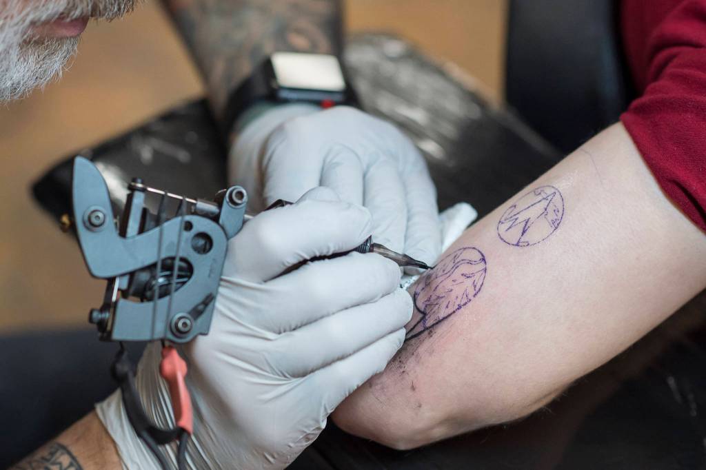 Tattoo artist Mario Singh applies a stylized semicolon to the back of Amy Ridles upper arm at Taku Tattoo on Monday, Nov. 19, 2018. (Michael Penn | Juneau Empire)