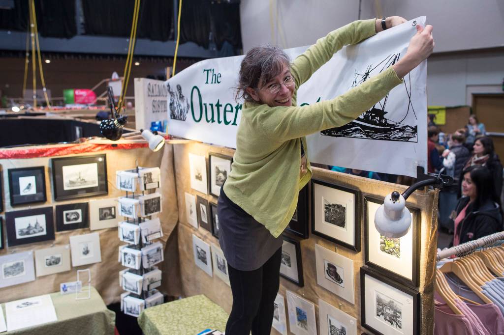 Rebecca Poulson ties up her sign The Outer Coast for her prints at the Public Market in Centennial Hall on Friday, Nov. 23, 2018. (Michael Penn | Juneau Empire)