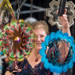 Marla Olsen hangs one of her wind spinners at the display booth she shares with her sister, Ruth, at the Public Market in the Elizabeth Peratrovich Hall on Friday, Nov. 23, 2018. (Michael Penn | Juneau Empire)