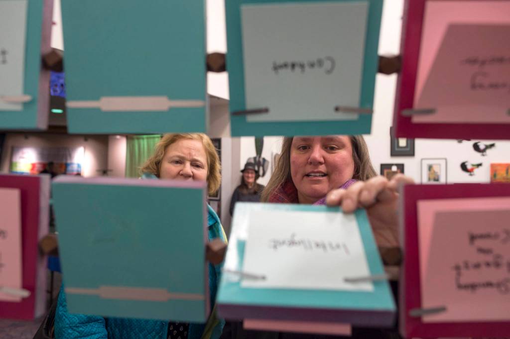 Cathy Needham, right, and Barb Sheinberg check out the The Rolodex Project//On Leadership by artist Sarah Campen, an interactive film and sculpture on display at The Davis Gallery in Centennial Hall during Gallery Walk on Friday, Dec. 7, 2018. (Michael Penn | Juneau Empire)