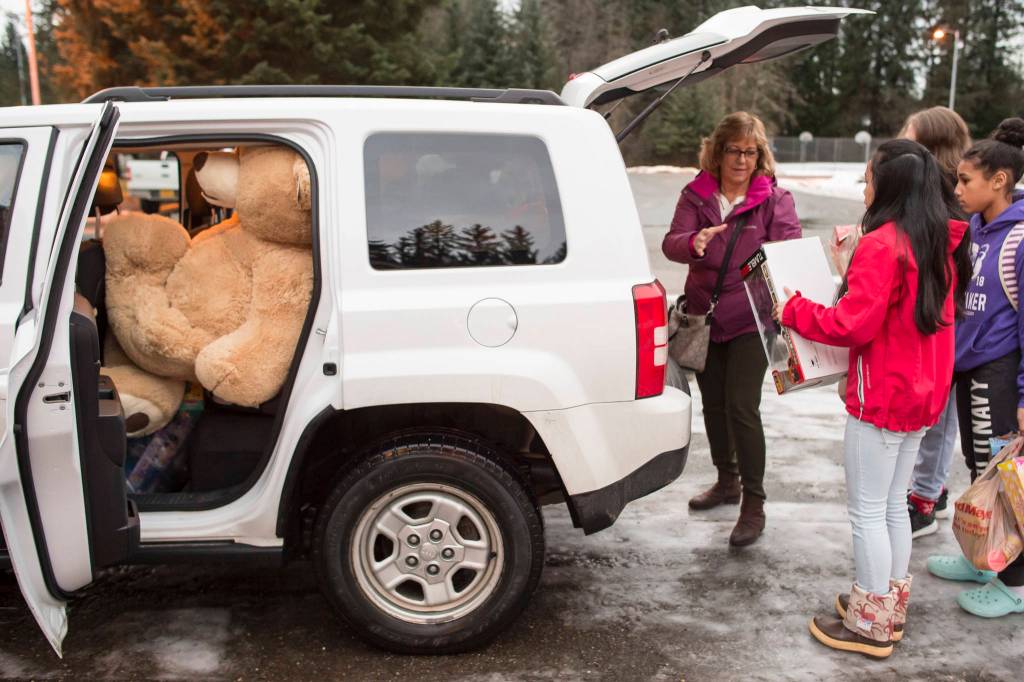 Lynn Logan, of the Alaska Department of Health and Social Services Office of Children Services, is helped load Christmas presents collected by Floyd Dryden Middle School student council members at FDMS on Monday, Dec. 17, 2018. The student organized a school money and toy drive for the OCS program to help needy children. (Michael Penn | Juneau Empire)