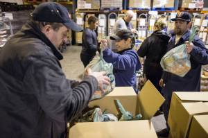 Super Bear/Foodland IGA employees Whitney Oudekerk, center, and Michael Stults, right, hand off bags of food for Super Bear IGA Director Tony Demelo to box at Super Bear IGA on Wednesday, Dec. 19, 20128, as part of the grocery stores Project 3 Squares. (Michael Pernn | Juneau Empire)