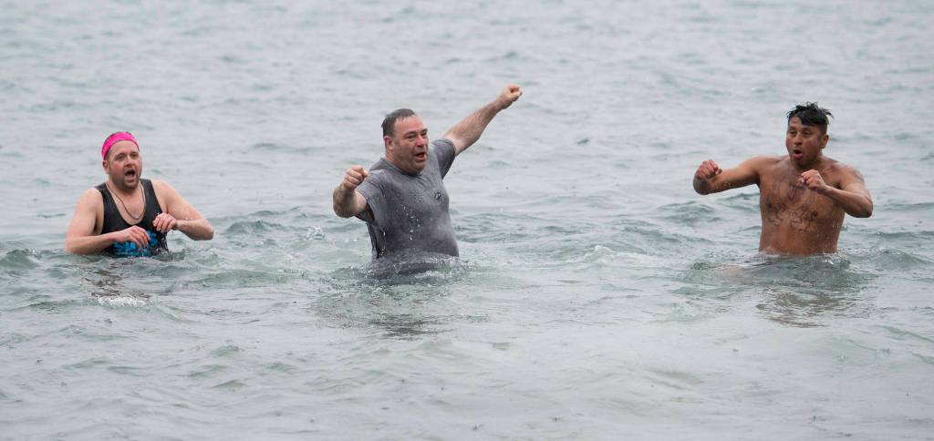 U.S. Coast Guard members John Dale, left, Chris Coutu, center, and Marvin Pena caught their breath after taking to the frigid waters at Auke Bay Recreation Area for the annual Juneau Polar Bear Dip on Tuesday, Jan. 1, 2019. Nearly 200 people took the plunge to start off the new year. (Michael Penn | Juneau Empire)