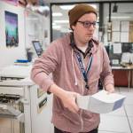 In this Sept. 25, 2018 photo, Mainframe Operator Will Muldoon lifts 500 freshly printed Permanent Fund Dividend checks from the printer at the states secure printing facility in Juneau. (Michael Penn | Juneau Empire)