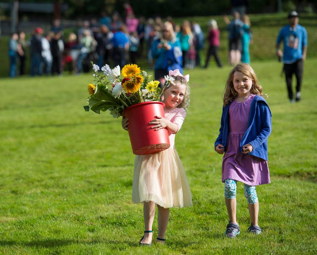 Juneau Community Charter School second-grader Elianna Amati, left, carries her classs flowers with third-grader Rebecca Frank after a ceremony at Evergreen Cemetery on the first of the school year on Monday, Aug. 20, 2018. (Michael Penn | Juneau Empire)