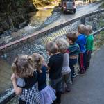 Children attending Fiddleheads Preschool line up along the fence at Cope Park to watch an excavator dredge Gold Creek on Wednesday, Sept. 12, 2018. (Michael Penn | Juneau Empire)
