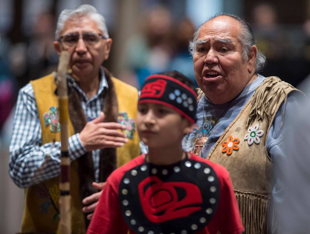 Tlingit elders David Katzeek, right, and Paul Marks, left, watch as Tyler Frisby, a member of the Tlingit Culture Language and Literacy Dance Group from Harborview Elementary School dance exits during the Voices of Our Ancestors Language Summit at Centennial Hall on Tuesday, Nov. 13, 2018. (Michael Penn | Juneau Empire)