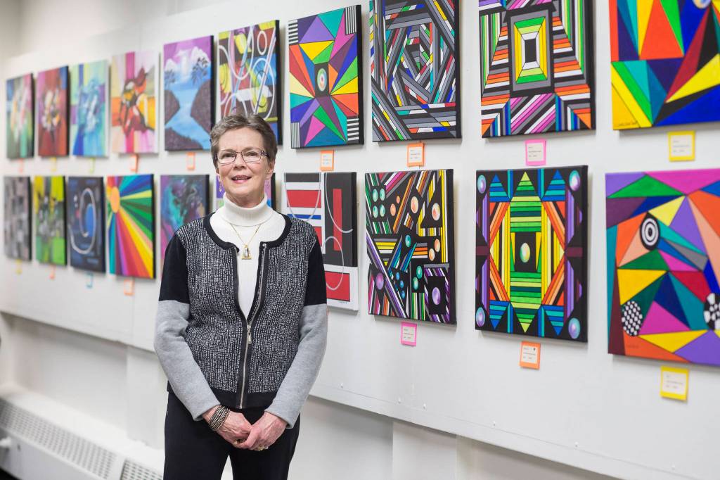 Carol Carlson stands with her paintings on display at the Juneau Arts & Humanities Council during First Friday on Friday, Jan. 4, 2019. (Michael Penn | Juneau Empire)