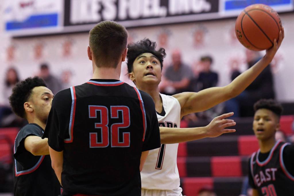 Juneau-Douglas Israel Yadao lays the ball up against East Anchorages Kaeleb Johnson, left, and Aiden Williams at JDHS on Friday, Feb. 8, 2019. East won 66-54. (Michael Penn | Juneau Empire)