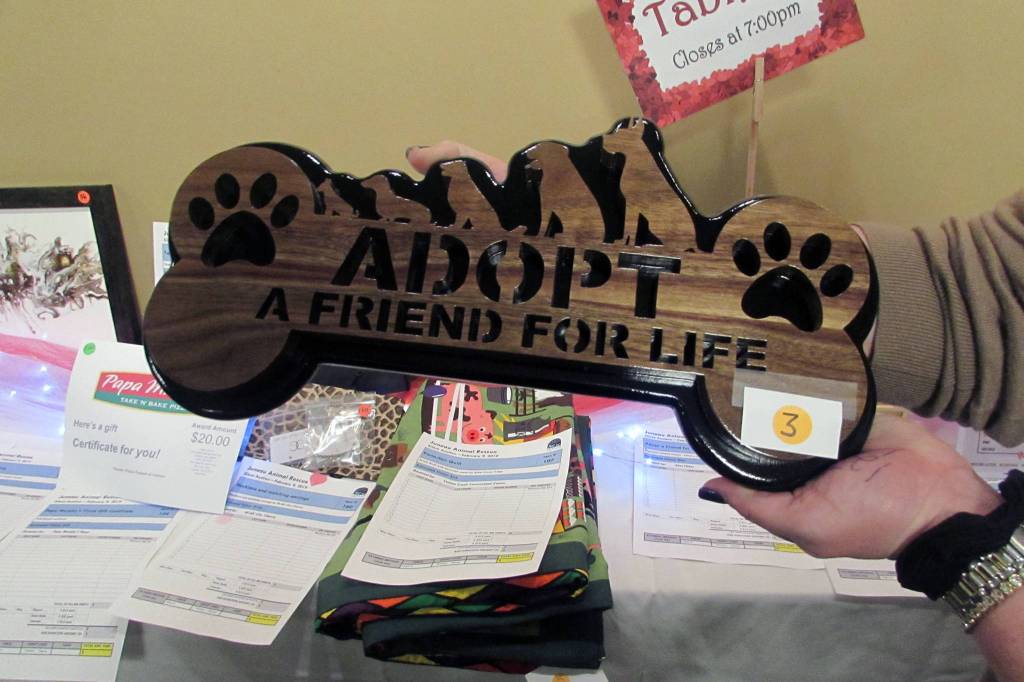 Mary Frances Fisher shows off a sign made by her husband, Alan. It was one of the items up for auction at a wine and beer tasting and silent auction benefiting Juneau Animal Rescue at the Westmark Baranof Hotel, Saturday, Feb. 9, 2019. (Ben Hohenstatt | Capital City Weekly)
