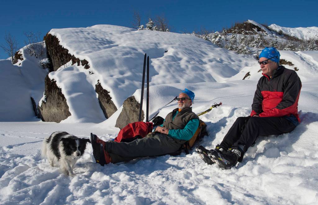Greg Cook, with his dog, Hibou, and Dr. John Connolly relax in the sun while out skiing at Mendenhall Lake on Monday, Feb. 11, 2019. (Michael Penn | Juneau Empire)