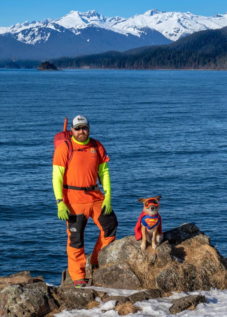March 17, 2019: Brian Weed, a seasoned outdoor adventurer and founding member of Juneaus Hidden History group, is a colorful character! He knows that bright colors are an important safety consideration when out exploring remote areas around Juneau. Brian wears orange North Face softshell pants, chartreuse Carhartt long-sleeve shirt, orange Underground Explorer T-shirt, red ArcTeryx backpack, Sly Fox hat, Lowa boots, Kahtoola microspikes and climbing gear. Kat  his dog  wears her equally colorful Super Girl cape and Rex Specs polarized dog goggles.